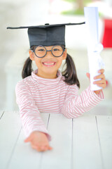 A little girl asia looks happy while celebrating his graduation and holding a diploma and graduation cap  which increases the development and enhances outside the classroom learning skills concept.