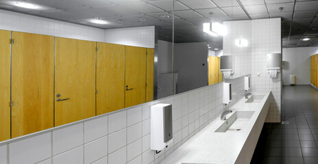Interior of a public restroom with sinks, faucets and toilet cubicles