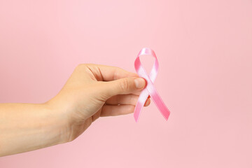 Female hand holds breast cancer awareness ribbon on pink background