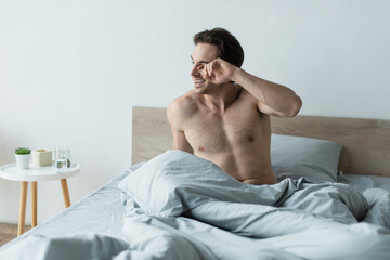 awake man smiling and rubbing eye on bed in morning