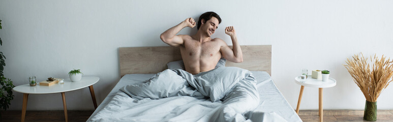 happy man stretching with closed eyes while sitting in bed, banner