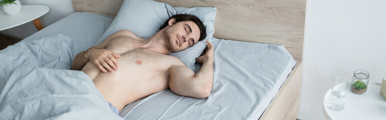 Fototapeta na wymiar shirtless man sleeping in bed near glass of water on bedside table, banner