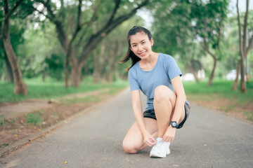Asian woman tying her shoelaces before going for a run in the park.