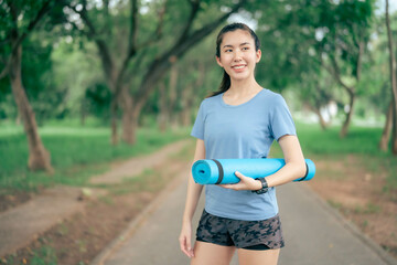 Asian women holding yoga mats are going to do yoga at the park to stay healthy and have good shape.