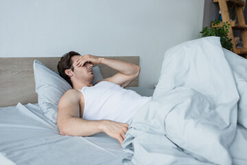 young man covering eyes with hand while lying in bed