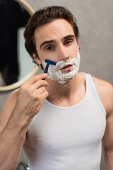 young brunette man looking at camera while shaving in morning