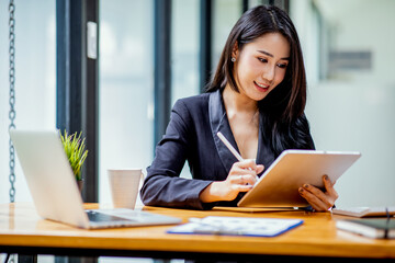 Portrait of Asian young female Businesswoman working on laptop computer doing finances,accounting analysis,report,data and pointing graph at the office.