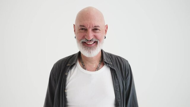 A smiling bald mature man posing to the camera standing isolated over white background in the studio