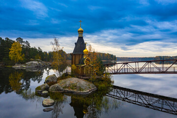 Churches Of Karelia. Orthodox shrines of Russia. Chapel on a rocky island in the middle of the lake. Chapel on the background of water and autumn trees. A bridge over the water leads to the Church.