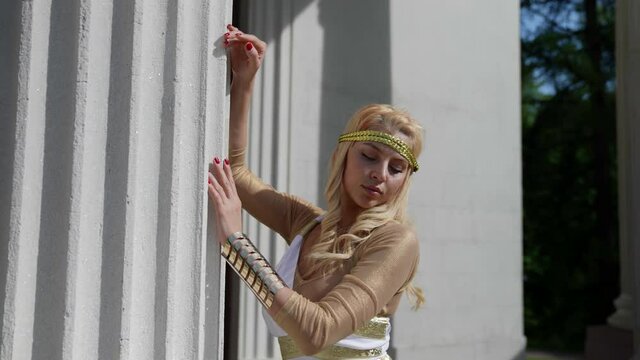 portrait of a blonde with big breasts and in a Greek chiton at the column. the camera is moving