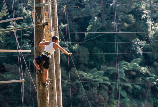 Man standing at top of poll ready to balance on suspended rope at outdoor ropes course