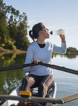 Female rower sitting in single scull canoe and drinking from bottle while having a break