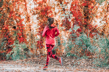 Running woman jogging on autumn red leaves foliage background. Fall cardio exercise training. Happy athlete runner exercising outdoor.