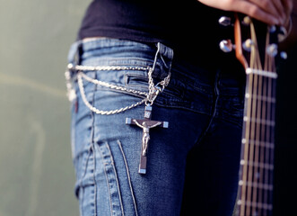 Mid section of young woman wearing a crucifix and chain around her waist and holding a guitar