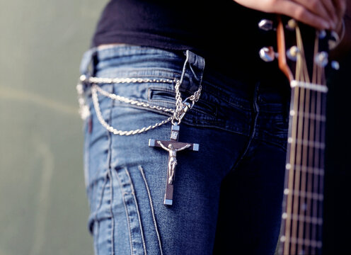 Mid section of young woman wearing a crucifix and chain around her waist and holding a guitar
