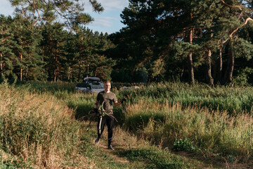 Photo of a Blond Man on a Summer Camping Activity with firewood for bonfire. Travel location of popular tourist outdoor. View of beautiful Forest Landscape. Vacation in the lake in a camp with a tent