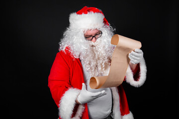 Charismatic Santa Claus reads letters. A man holds a scroll in his hands. Black background.