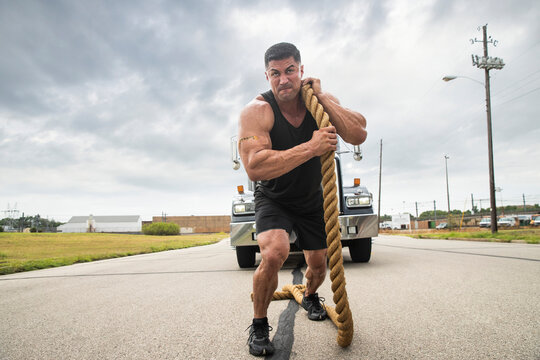 Muscular Hispanic man wearing tank top with Strong tattoo on his bicep, Pulling semi truck with large tow rope 