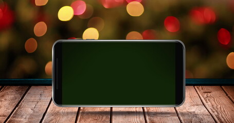 Image of blank smartphone screen on wooden surface over flickering fairy lights