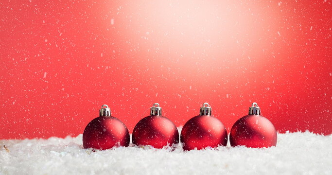 Image of christmas baubles decorations with snow falling on red background