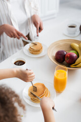 partial view of african american woman with daughter cutting croissants during breakfast