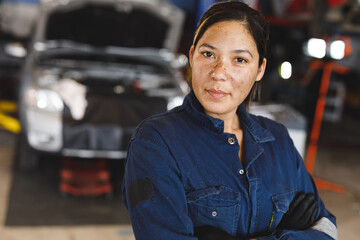 Mixed race female car mechanic wearing overalls, looking at camera