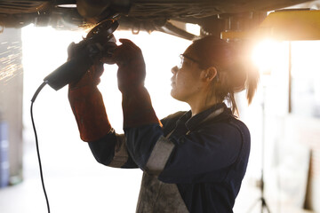 Mixed race female car mechanic wearing overalls, using angle grinder