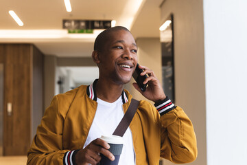 Smiling african american male business creative using smartphone and holding coffee
