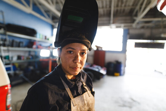 Mixed race female car mechanic wearing overalls and welding mask, looking at camera