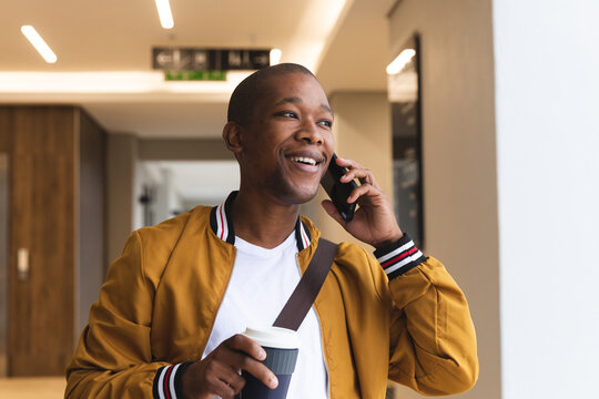 Smiling african american male business creative using smartphone and holding coffee