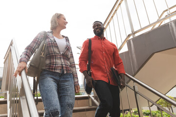 Smiling diverse female and male colleagues walking downstairs outside office and talking