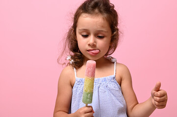 Headshot 4 years pretty baby girl with healthy vegan ice cream popsicle in hand and showing thumb...
