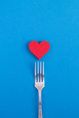 Red heart and silver fork on the blue background. Copy space.Top view.
