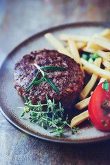 Hamburger steak with french fries and tomatoes. Brown stone background. Close up.	