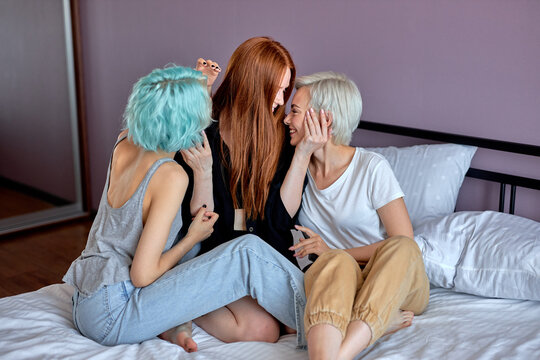 Threesome concept. Three awesome lesbian ladies in domestic clothes sit on bed flirting, hugging, women in love, lesbian, same sex females enjoy spending time together, going to have sex. side view