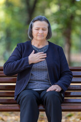 Senior lady clutching her chest in pain in park on an autumn day