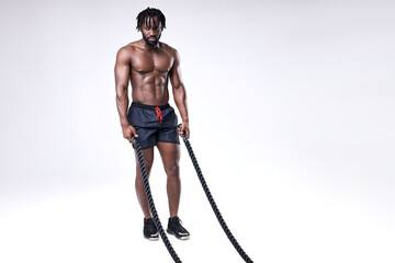 Fototapeta na wymiar slim well-built afro american athlete preparing for training with battle ropes, full-length portrait, isolated white background, studio shot. bodybuilding, cross fit, weightlifting, sport, fitness