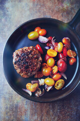 Fried hamburger steak with various cherry tomatoes and fresh herbs. Rustic background. Top view.	