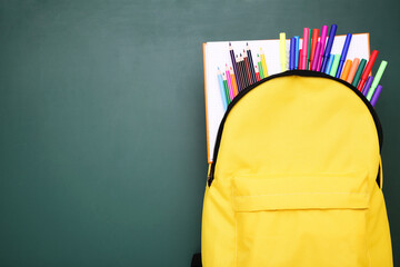 Backpack with school supplies on green background