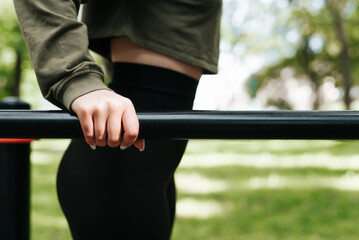 Fototapeta na wymiar Athletic fit woman doing physical exercise, push-ups on parallel bars. Selective focus on female hand holding bar outdoors, close-up. Women's strength training