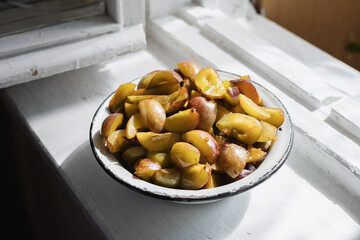 fresh ripe slices of pitted plums lie in a metal bowl on a white windowsill