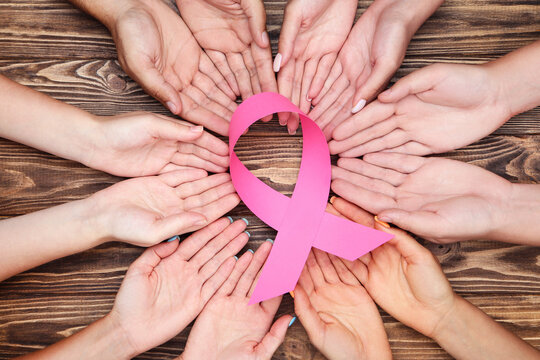 Breast cancer concept. Group of people in hands holding pink paper ribbon on brown wooden table