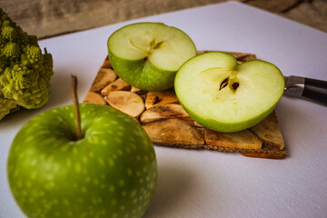 Tasty food in green. Two apples: one is whole, the other cut into two parts. Broccoli in a strange pyramid shape. Knife and board for cutting made of wood.