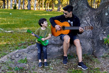 Latin father and son playing guitar and ukelele together sitting i a tree in a forest in Argentina....
