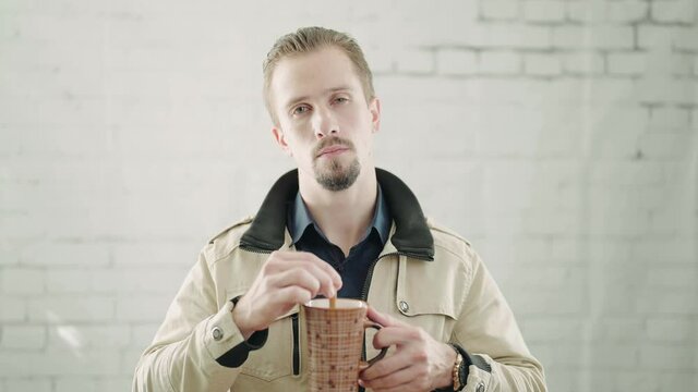 Man portrait mixing coffee mug and listening to you with serious expression 4K
