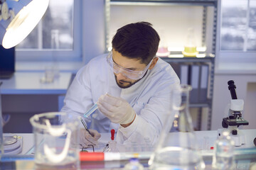Male scientist working at analytics chemical laboratory comparing sample in glass tube with test paper indicator. Chemist research work in micrological science clinical lab. Bio chemistry and medicine