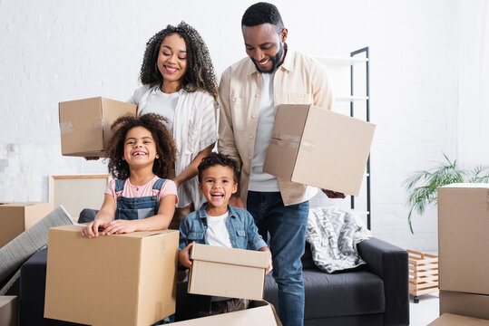 excited african american family holding cardboard packages in new apartment