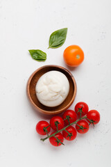 Delicious fresh cheese made from cream and milk - burrata. Italian tender cheese with tomatoes in a wooden plate on a light background