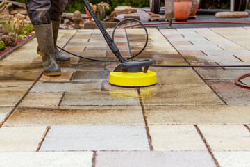 Cleaning stone slabs on patio with the high-pressure cleaner. Person worker in rubber boots...