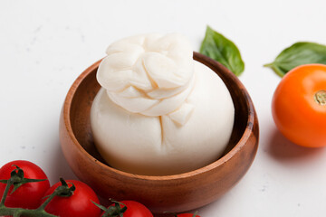 Delicious fresh cheese made from cream and milk - burrata. Italian tender cheese with tomatoes in a wooden plate on a light background